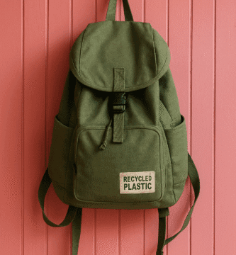 mochila verde hecha con plástico reciclado colgada de pared rosa